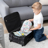 A young boy places Bumkins Packing Cube 2 Pack: Mickey & Friends Varsity into a black suitcase on the living room floor.