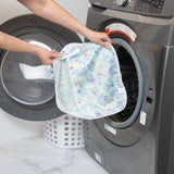 A person holds a Bumkins Packing Cube 2 Pack: Aloha Stitch in front of an open washing machine next to a white laundry basket.