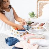 A girl in a white dress uses the Bumkins Packing Cube 2 Pack: Winnie + Friends to organize clothes on a bed.