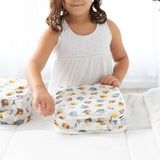 A child in a white dress zips Bumkins Packing Cube 2 Pack: Winnie + Friends on a white bed.