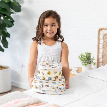 A smiling girl by a bed holds bags from Bumkins The Outfit Organizer Essential 5-Piece Set: Winnie and Friends.
