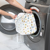 A person holds a Bumkins Packing Cube 2 Pack: Winnie + Friends in front of a front-loading washing machine.
