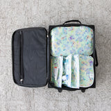 Open suitcase on gray carpet, neatly packed with Bumkins Aloha Stitch packing cubes and clear travel bags for toiletries.