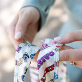 Close-up of hands holding a Bumkins Packable Tote Bag: Mickey & Friends Varsity featuring a snap button closure.