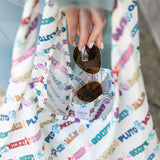 Close-up of a hand placing sunglasses into the pocket of Bumkins Packable Tote: Mickey & Friends Varsity.