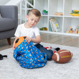 A child packs a soccer ball into a blue Bumkins Packable Tote Bag: Mickey & Friends Forever, with a football nearby on the rug.