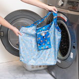 A person holds a Bumkins Packable Tote Bag: Mickey & Friends Forever in front of an open washing machine.