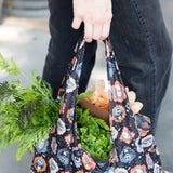 A person holds a Bumkins Packable Tote Bag: Ghostly Gallery with fresh greens, featuring a Nightmare Before Christmas design.