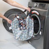 A person holds a Bumkins Packable Tote Bag: Ghostly Gallery in front of an open front-loading washing machine.