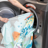 A person loads a Bumkins Reversible Roll & Go Blanket, Rolling with the Waves into a front-loading washing machine.