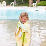 A child smiles by the pool, wrapped in a Bumkins Reversible Roll & Go Blanket, Happy Camper.