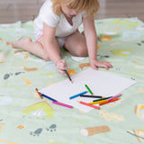 A child drawing with colored pencils on a Bumkins Reversible Roll & Go Blanket, Happy Camper—ideal for creative times indoors or outdoors.