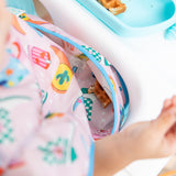 Close-up of a child in a Bumkins Ruffle Apron Bib: Boots, with focus on a piece of waffle in the pocket.