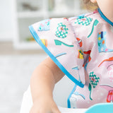 Close-up of a child wearing a Bumkins Ruffle Apron Bib: Boots in a high chair, with focus on the bib's ruffle sleeve.