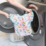 A person holds Bumkins Ruffle Apron Bib: Boots in front of an open front-loading washing machine.