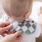 Close-up of a person adjusting the hook-and-loop closure of a Bumkins SuperBib® 3 Pack: Palms + Check on a seated baby.