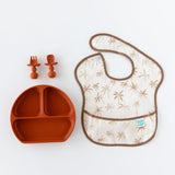 A palm tree Bumkins SuperBib® 3 Pack: Palms + Check, rust-colored plate, and two matching utensils are displayed on a white background.