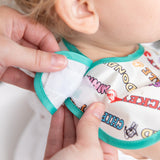 Close-up of a person fastening the hook and loop closure of Bumkins SuperBib® 3 Pack: Mickey & Friends MVP on a toddler.