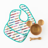 A white Bumkins SuperBib® 3 Pack: Mickey & Friends MVP lays next to a gold bowl and matching spoon on a white background.