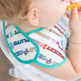 A toddler enjoys an orange slice wearing a colorful Bumkins SuperBib® 3 Pack: Mickey & Friends MVP.