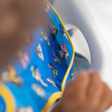 A child in a high chair wearing a blue Bumkins SuperBib® 3 Pack: Mickey & Friends MVP, with focus on the pocket.