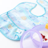 A Bumkins SuperBib® 3 Pack: Stitch Star-ring Up Trouble lays flat next to a purple bowl filled with yogurt and berries.