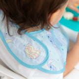 A child in a Bumkins SuperBib® 3 Pack: Stitch Star-ring Up Trouble sits in a high chair next to a blue plate.