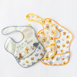 Bibs from Bumkins On-The-Go Mealtime 7-Piece Set: Pooh Bear + Friends lay overlapped on a white background.