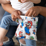 A person reaches into a Bumkins Reusable Snack Bag, Large: Super Mario™ & Luigi while a baby sits on their lap.