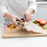 A person places a sandwich into a Roamio by Bumkins Bumkins Reusable Snack Bag, Large 2 Pack: Double Check on a cutting board with vegetables.