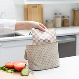 A hand places a Roamio by Bumkins Bumkins Reusable Snack Bag, Large 2 Pack: Double Check in a lunch bag on a kitchen counter next to veggies.