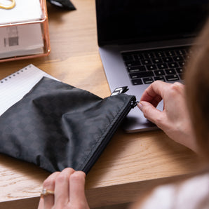 A person unzips a black Roamio by Bumkins Reusable Snack Bag, Large 2 Pack: Rich & Boujee at a desk with work essentials.