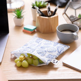 A Roamio by Bumkins Reusable Snack Bag, Large 2 Pack: Coastal holds green grapes on a desk near a coffee cup, notebook, & office supplies.