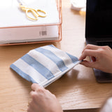 Close-up of hands holding a Roamio by Bumkins Reusable Snack Bag, Large 2 Pack: Coastal near a laptop and papers on a desk.