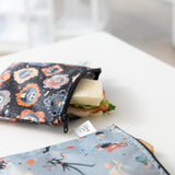 A Bumkins Reusable Snack Bag, Large 2 Pack: Everyday Is Halloween holds a sandwich on a white table.