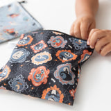 A child opens a Bumkins Reusable Snack Bag, Large 2 Pack: Everyday Is Halloween at a white table.