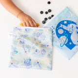 A child's hand reaching into a Bumkins Reusable Snack Bag, Large 2 Pack: Stitch Star-ring Up Trouble, with blueberries nearby.