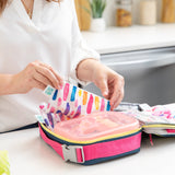 A woman packs a lunch bag with Bumkins Lunchbox Legends 6-Piece Set: Watercolor Pink Jelly on a kitchen counter.
