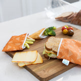 Bumkins Reusable Snack Bag 4 Pack: Desert Boho holds snacks, veggies and a sandwich on a wood cutting board on a kitchen counter.