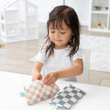 A young girl with a white bow opens a Bumkins Reusable Snack Bag, Small 2 Pack: Double Check at a white table with another bag nearby.
