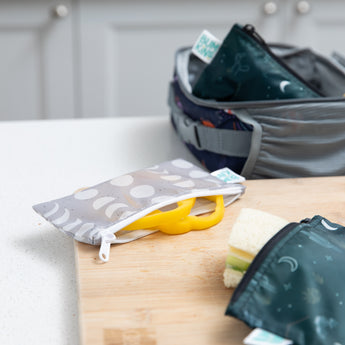 A Bumkins Reusable Snack Bag, Small 2 Pack: Desert Night rests on a cutting board with yellow bell pepper slices peeking out.