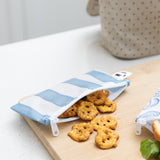 A Bumkins Reusable Snack Bag, Small 2 Pack: Coastal holds pretzels on a wood cutting board on a kitchen counter.