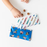 A child's hand reaches for treats near Bumkins Reusable Snack Bag, Small 2 Pack: Mickey & Friends MVP on a white table.