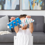In a cozy living room, a child holds two Bumkins Reusable Snack Bag, Small 2 Pack: Mickey & Friends MVP in front of their face.