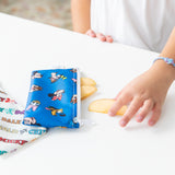 A child reaches for apple slices next to Bumkins Reusable Snack Bag, Small 2 Pack: Mickey & Friends MVP on the white table.