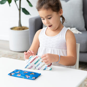 A girl eagerly opens Bumkins Reusable Snack Bag, Small 2 Pack: Mickey & Friends MVP at a white table.
