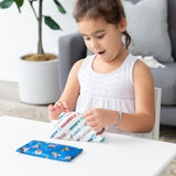 A young girl smiles as she opens a Bumkins Reusable Snack Bag 4 Pack: Disney Mickey & Friends Crew at a white table indoors.