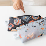 A child holds a cookie near Bumkins Reusable Snack Bag, Small 2 Pack: Everyday Is Halloween on a white table.