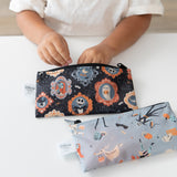 A child reaches into a Bumkins Reusable Snack Bag, Small 2 Pack: Everyday Is Halloween on a white table with another bag nearby.