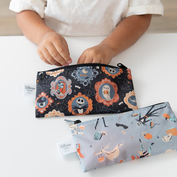 A child reaches into a Bumkins Reusable Snack Bag, Small 2 Pack: Everyday Is Halloween on a white table with another bag nearby.